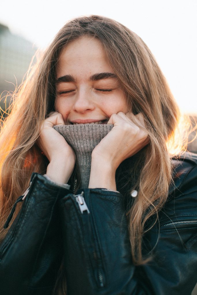 Shy woman pulling her shirt neck up with closed eyes